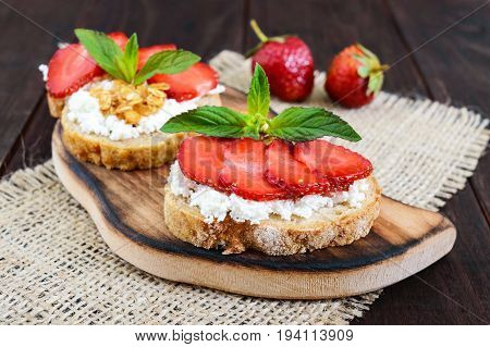 A small bruschetta with curd and fresh strawberries on a dark wooden background. Proper nutrition.