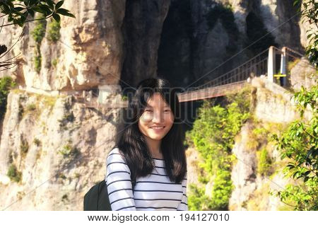 A chinese woman smiling with the Fangdong suspension bridge spanning a sheer cliff in the background in the yandangshan scenic area in Zhejiang province China.