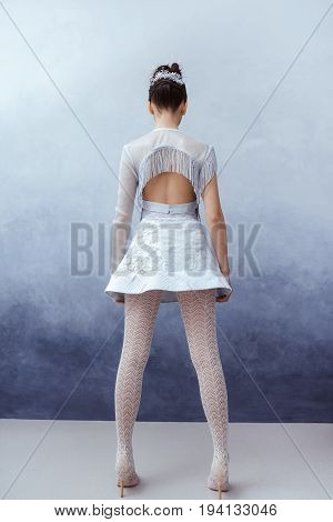Futuristic fashion young woman. Beautiful young multi-racial asian caucasian model girl in silver urban clothes with conceptual hairstyle and make-up against textured blue wall in full lenght. Back view. Sci-fi poster style.