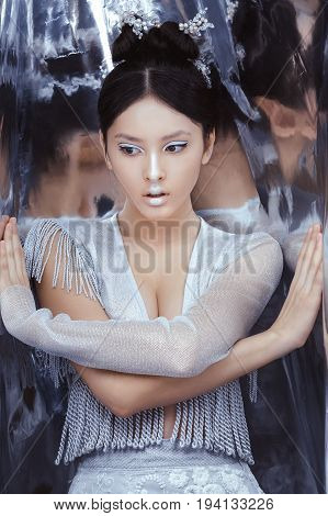 Portrait of futuristic young woman. Reflection of our mind and soul concept. Beautiful young multi-racial asian caucasian model cyber girl in silver urban clothes with conceptual hairstyle and make-up in metallik silver capsule.