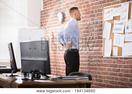 Businessman Leaning Against The Brick Wall Having Back Pain In Office