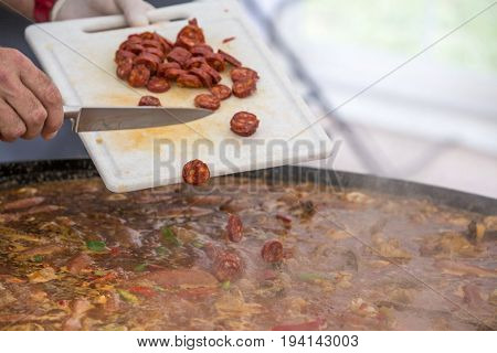 Cooker putting chorizo sausage pepperoni in paella jumbalaya louisiana country plate