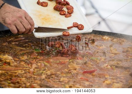 Cooker putting chorizo sausage pepperoni in paella jumbalaya louisiana country plate