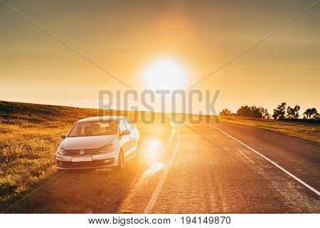 Gomel Belarus - August 25, 2016: Sun Rising Over VW Volkswagen Polo Vento Sedan Car Parking Near Asphalt Country Road In Sunny Morning Or Evening. Open Road At Sunny Sunset Or Sunrise Time At Summer