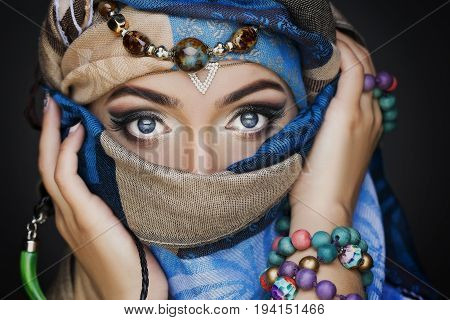Portrait of young beautiful woman close up. Perfect makeup. Perfect skin. Fashion photo.Beauty lady with colored turban over blue background