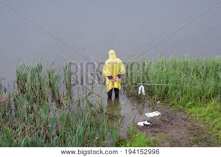 Yoshkar-Ola Russia - June 14 2017 A photograph of a fisherman in a raincoat fishing in the rain which stands in knee-deep in the river Kokshaga