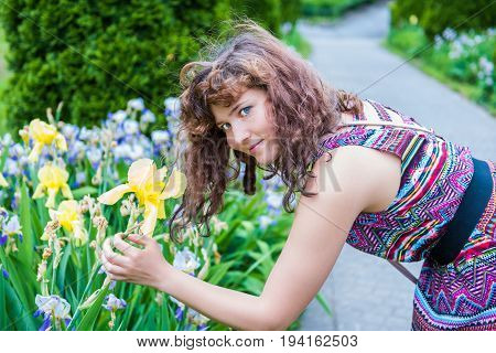 Young woman holding and smelling yellow iris flowers in park during summer outside