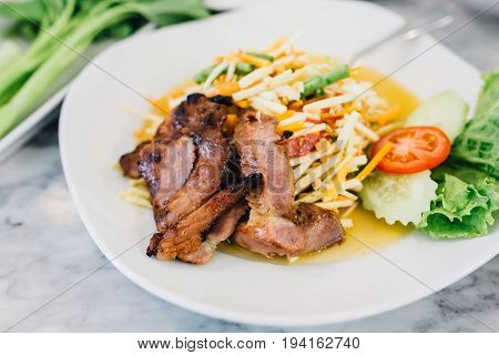 Papaya Salad with Grilled Pork Neck on white plant.