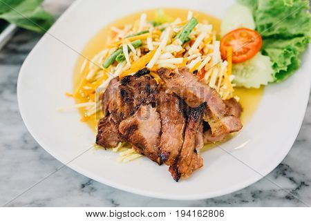 Somtum roasted pork neckon a white plate , Thai food.