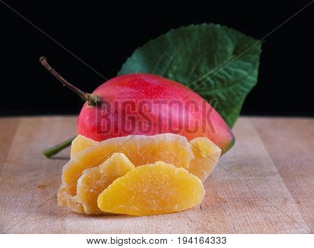 Detail of dried mango slices with whole ripe fruit on wooden background