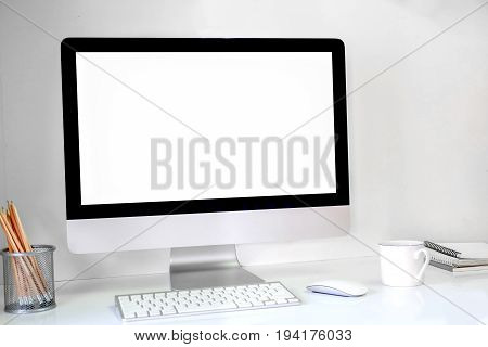 Creative hipster desktop with blank white computer screen coffee cup and other items on white brick background. Mock up workspace.