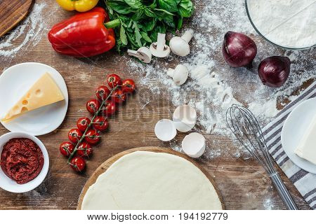 Top View Of Unbaked Pizza Dough With Fresh Ingredients On Wooden Table