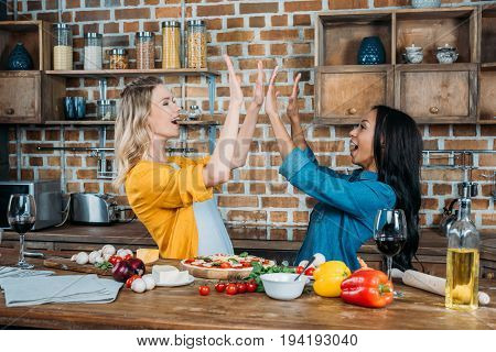 Cheerful Young Miltiehnic Women Giving High Five While Cooking In Kitchen