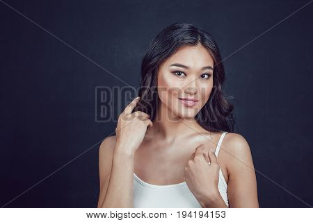 Portrait of a beautiful asian woman with makeup and light curls on black background.