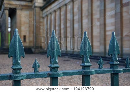 A vintage iron fence with greenish spearheads guards the approach to a historic stone building in Edinburgh Scotland.