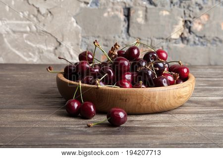 Fresh cherry in a wooden plate on an old wooden background. New harvest. Gardening. Ingredient for cooking and vegetarian food. Healthy eating.
