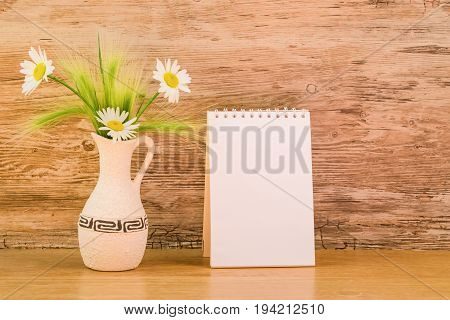 Mocap, background from a blank white sheet of paper in a notebook near bright plastic walls and ceramic vase with daisies on a wooden table, mock up