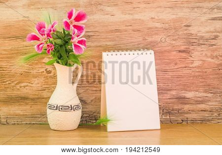 Mocap, background from a blank white sheet of paper in a notebook near bright plastic walls and ceramic vase with pink and purple garden flowers on wooden table, horizontal, mock up
