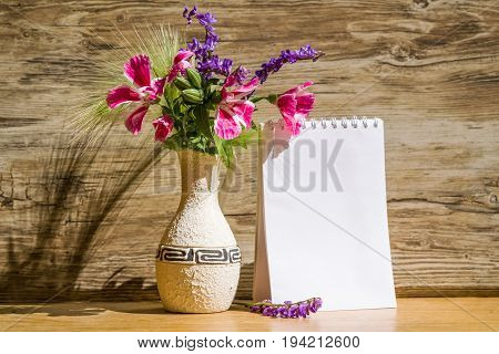 Mocap, background from a blank white sheet of paper in a notebook near bright plastic walls and ceramic vase with pink and purple garden flowers on wooden table with shadow, sunlit, horizontal, mock up