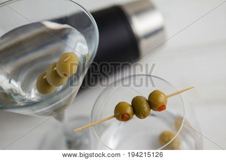 Close up of olives in vodka martini with cocktail shaker in background