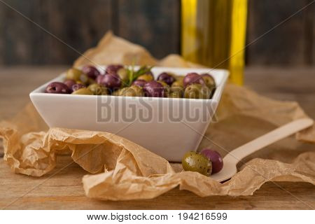 Close up of olives served in bowl by wooden spoon on wax paper
