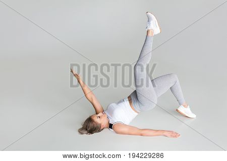 Blonde woman wearing white top and pants holding right leg up lying on floor.