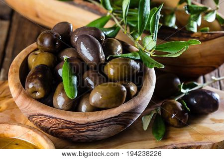 Olives and olive oil in olive wooden bowls on olive wooden cutting board, olive tree branch on wooden rustic background