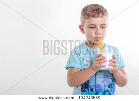 Close-up portrait of charming little boy with a glass full of organic milk on a gray background. A nice little boy holds a glass of fresh milk on gray background. Healthy products. Dairy products.