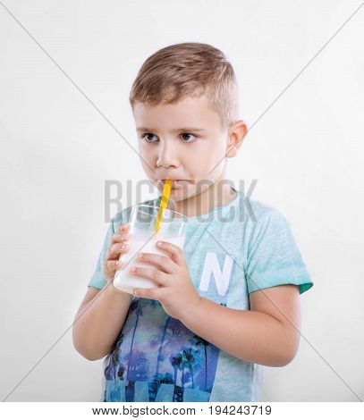 Pretty little boy is drinking milk in a glass from a yellow straw. Close-up portrait of cute little kid is drinking milk from yellow straw in the morning on gray background. Concept of healthy living, food  drink, family.