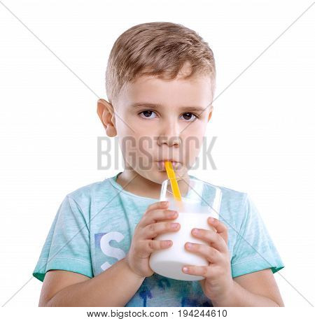 A beautiful little kid in a blue T-shirt with a glass of a tasty milk. Delightful little baby boy is drinking fresh milk from a bright yellow straw. Close-up portrait of amazing boy drinks a glass of milk isolated on white background.
