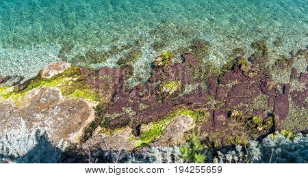 A colorful rocky coastline in Corfu. Clean blue water and rocks covered by moss