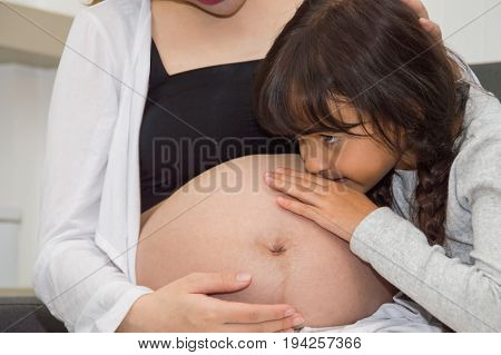 The girl is listening to belly of pregnant mother