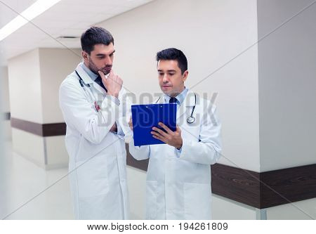 medicine, healthcare and people concept - two male doctors with clipboard at hospital corridor