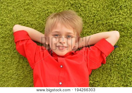 Portrat of blonde little boy lying on green carpet in room