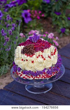 birthday cake with chocolate ganache decorated with roses lavender and berries, garden with flowers in the background