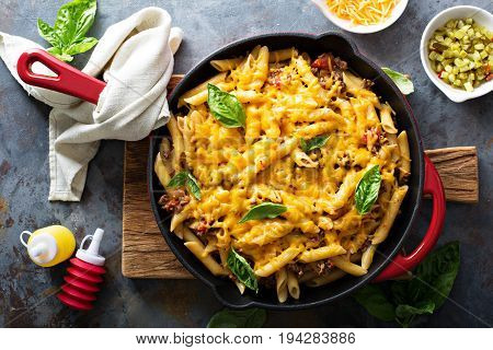 Cheesy pasta bake in a pan with ground beef and herbs overhead shot
