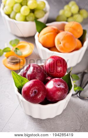 Various fresh tasty fruits in white bowls with plums, apricots and grapes