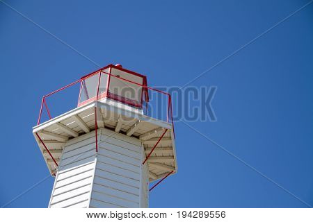 Lantern on a hexagonal white lighthouse or pharos for marine navigation and to warn of hazards such as rocks and shoals viewed close up from below against a blue sky
