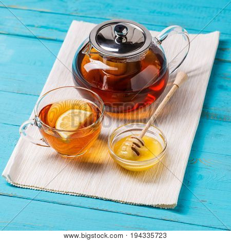 Glass cup of tea with lemon, glass teapot and honey on blue wooden table.