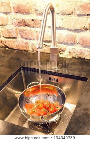 Closeup of tomatoes in colander under running water in sink