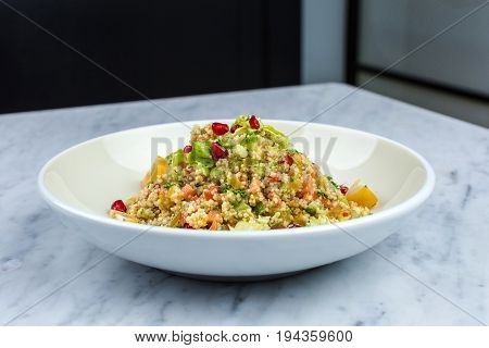 Quinoa salad with pomegranate in white plate on marbel decks