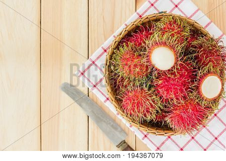 fresh tropical rambutan fruits over basket with knife on wood background Top view with copy space and text.
