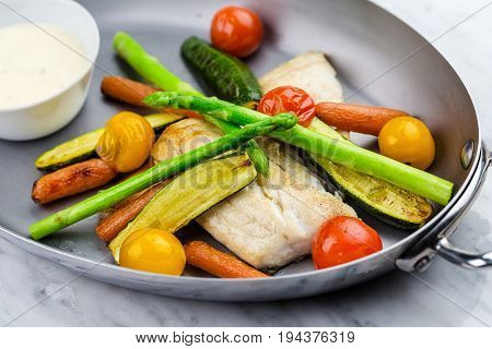 Grilled fish and vegetables with sauce served in metalic bowl on marble serface