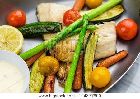 Grilled fish and vegetables with sauce served in metalic bowl on marble serface