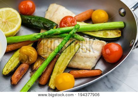 Grilled fish and vegetables with sauce served in metalic bowl on marble serface