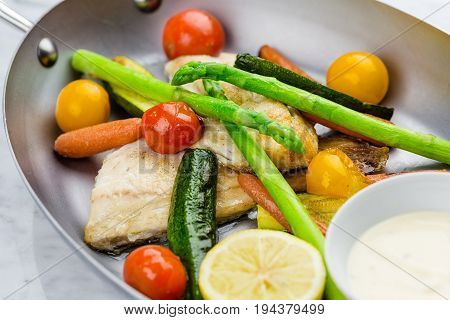 Grilled fish and vegetables with sauce served in metalic bowl on marble serface