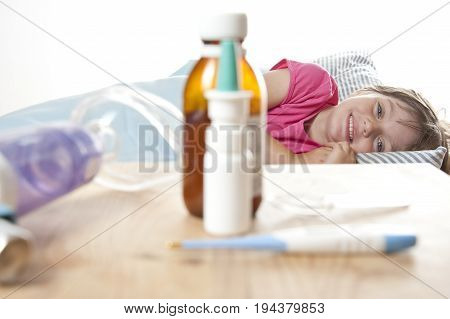 ill little girl in her bed and drugs inhaler and thermometer
