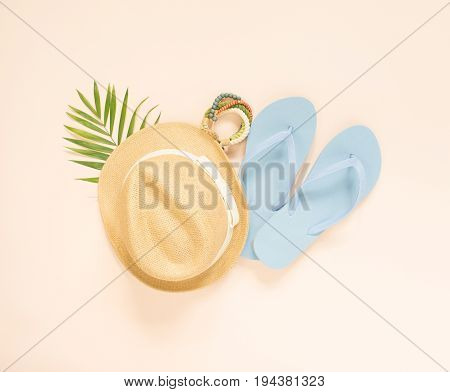 Summer fashion summer outfit on cream background. Blue flip flops seashell wood bracelet and straw hat. Flat lay top view