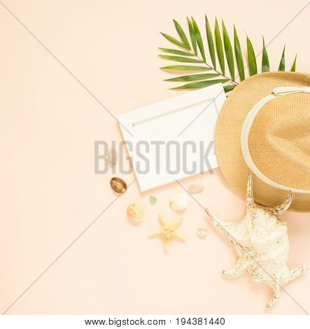 Empty frame and summer holidays items on creme background. Straw hat seashells and starfish. Selective focus. Place for text. Flat lay top view.