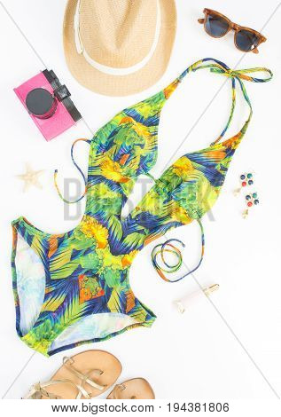 Summer outfit beach outfit summer stuff. Exotic pattern swimsuit retro sunglasses gold sandals pink retro camera and straw hat. Flat lay top view.